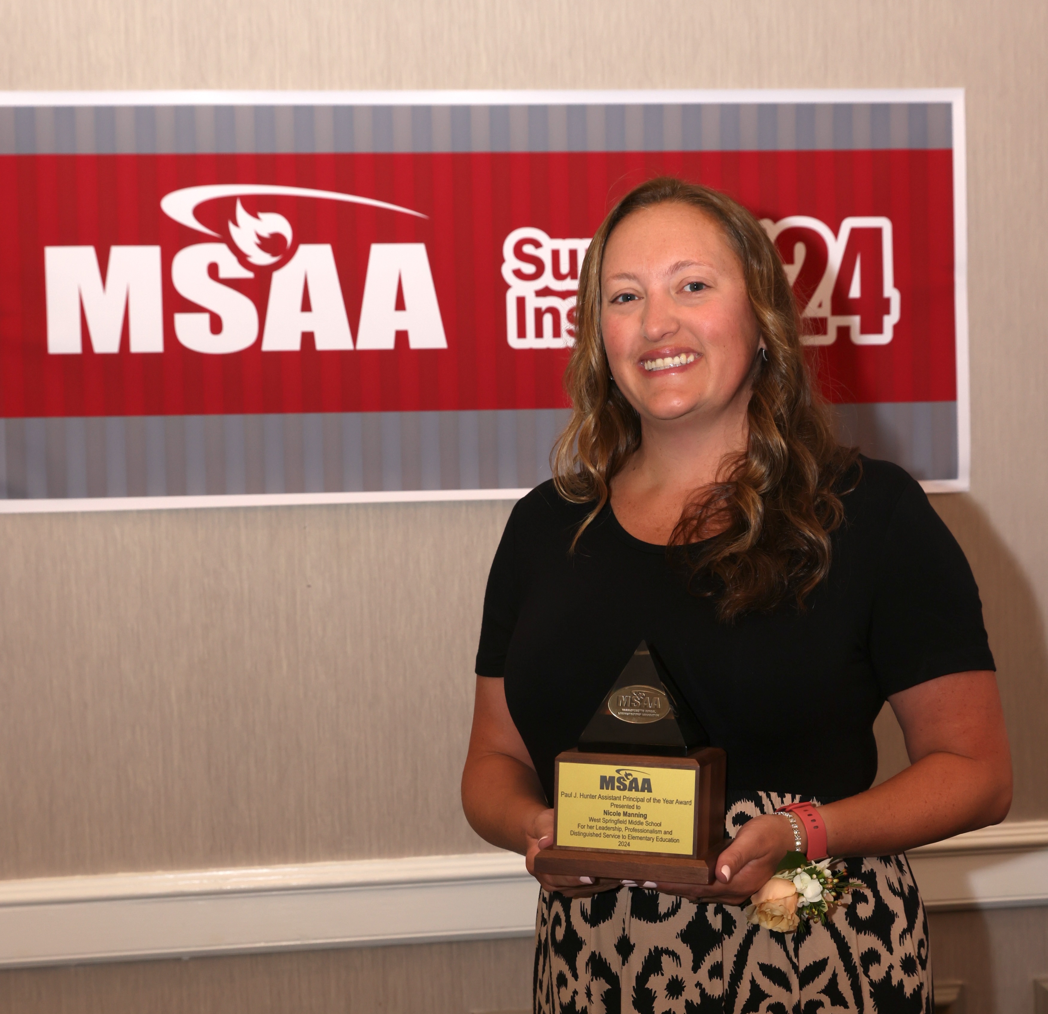 a woman stands in front of a msaa sign, holding an award.